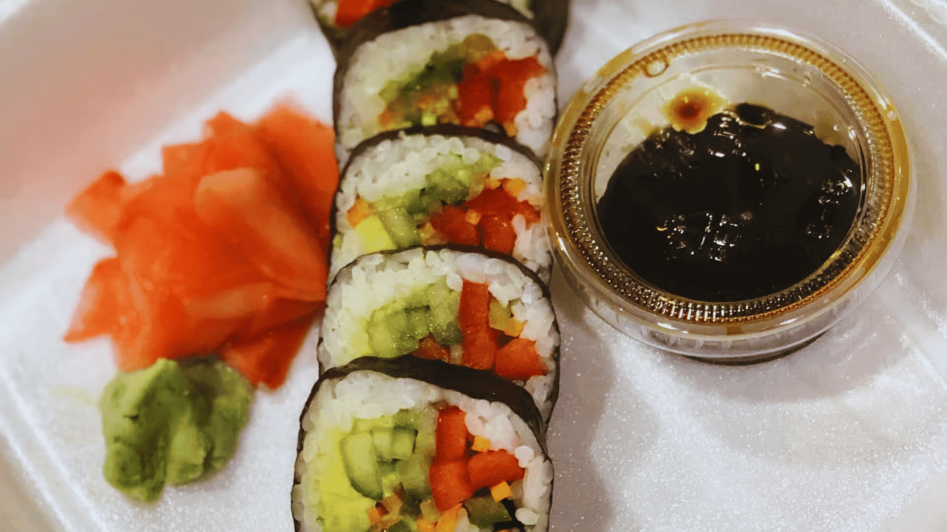 Vegetable sushi rolls with pickled ginger, wasabi, and soy sauce in a takeout container.